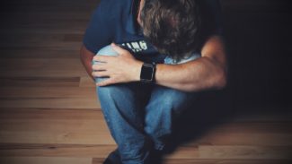 Image of man sat on the floor, with his knees bent up and hiding his face