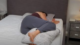 Person lying on their side in bed with a pillow between their knees