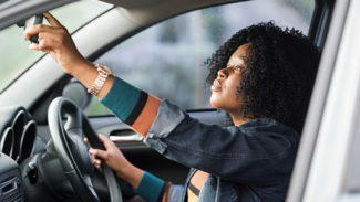 Person sat in the drivers seat of a car, adjusting the rear view mirror