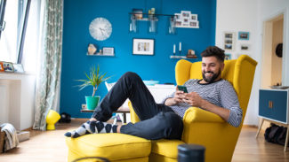 Image of a man reading from his phone and smiling, while sat in an arm chair