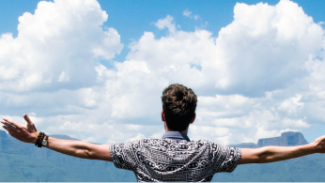 Man facing away from the camera, reaching his arms towards the blue but cloudy sky