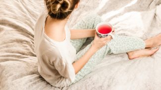 woman sat on bed holding a mug while looking away from the camera