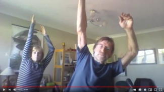 Screenshot of zoom video showing Ian and Andrea reaching their arms up and leaning to their left