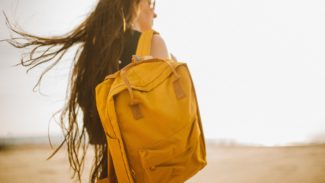 Woman with brown hair and glasses wearing a yellow backpack looks away from the camera