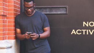 Man stands looking down at the mobile he's holding in his hands