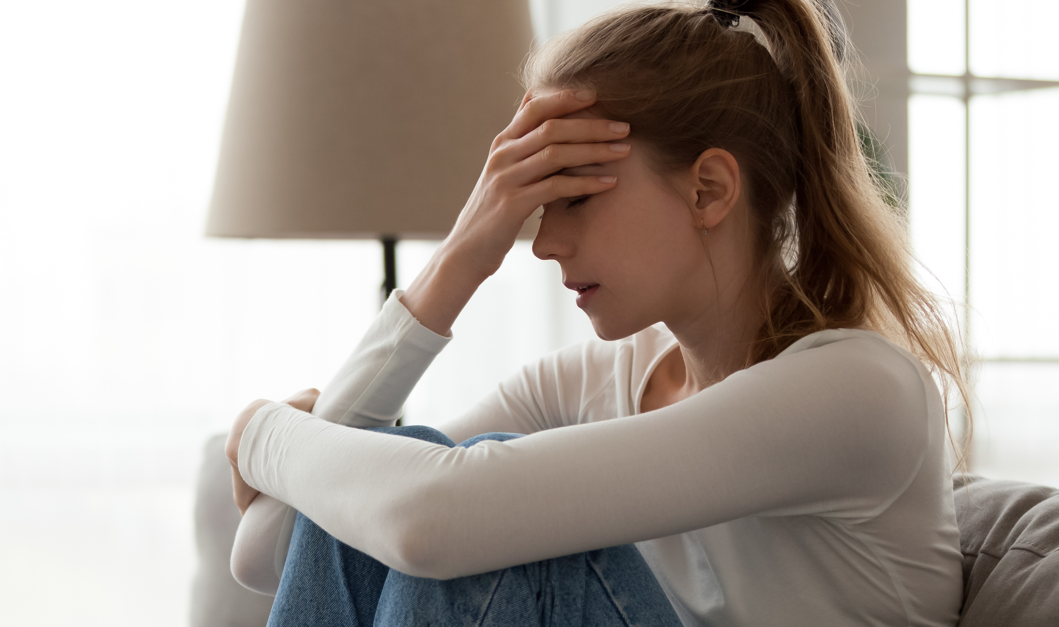 Upset woman frustrated by problem sitting on couch, embracing knees,