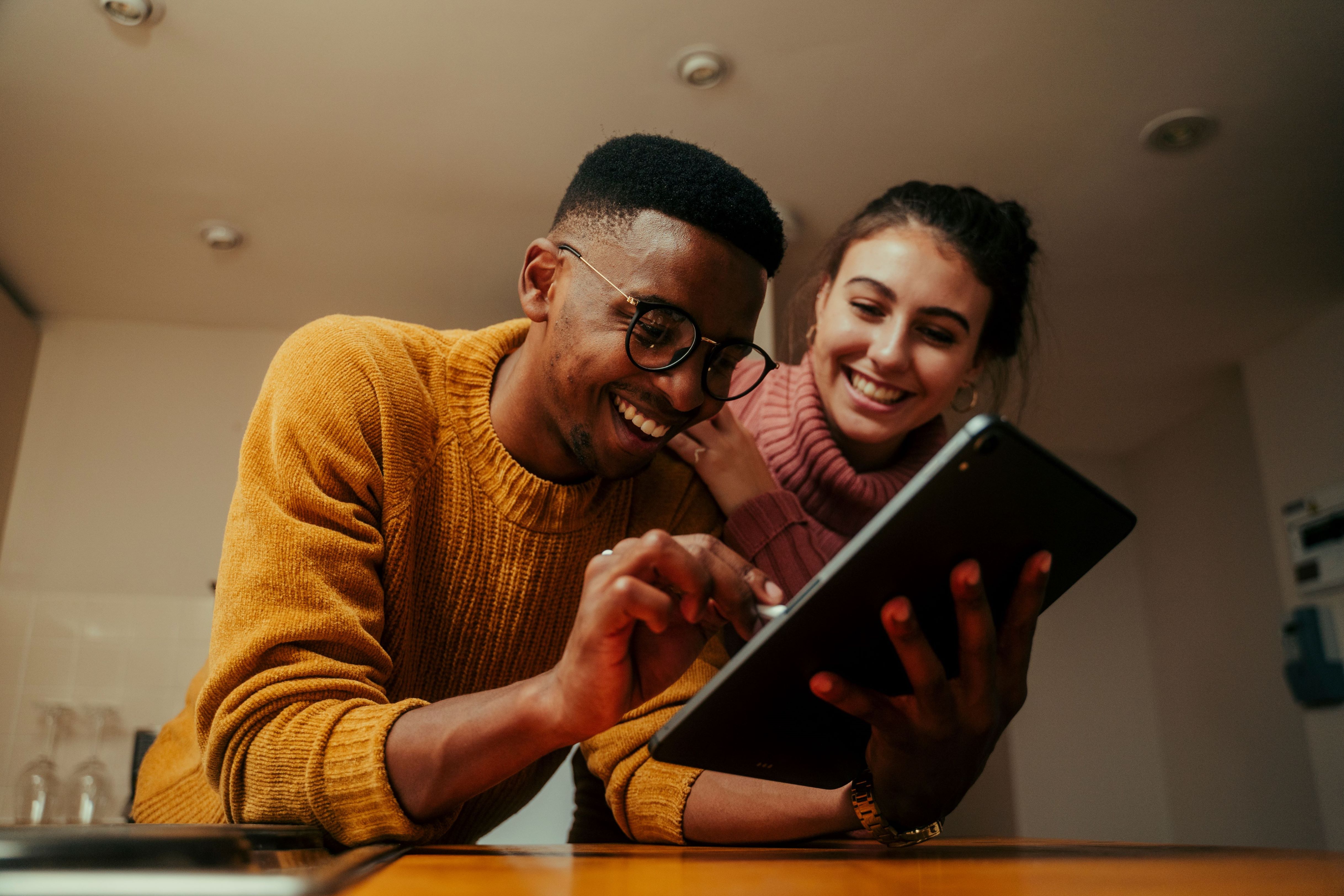 A man and a woman are smiling as the man uses an ipad to discover ways to manage his axial spondyloarthritis symptoms